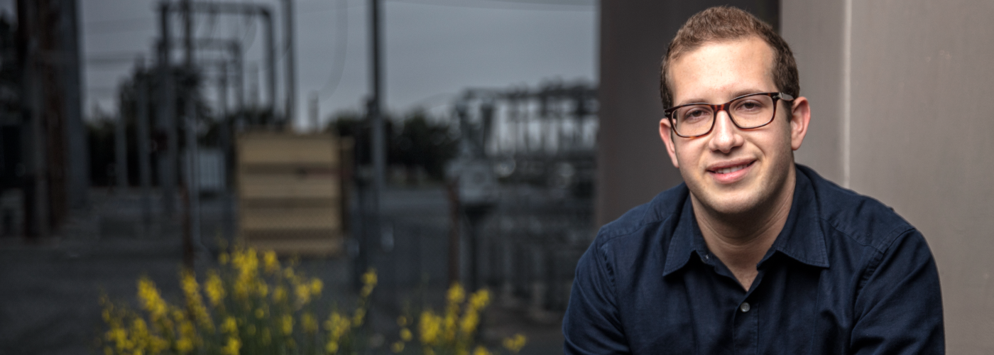 A smiling young man with glasses looking at the camera