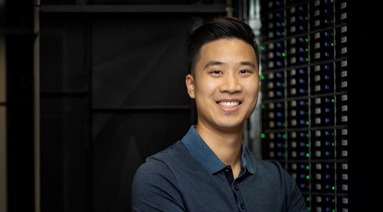 A man smiling facing the camera with a computer machine in the background
