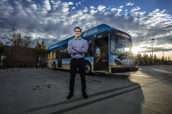 A man with arms crossed looking towards the camera with en electric powered bus in the background