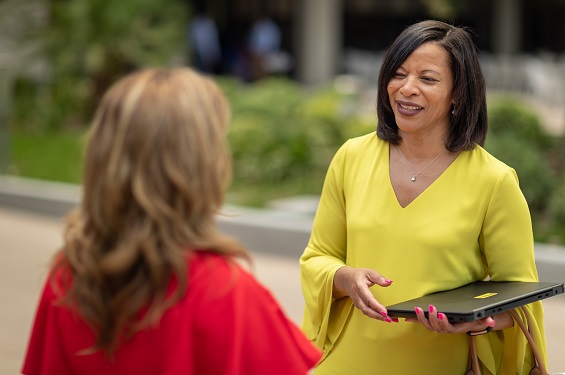 A woman outside talking to another woman with a laptop in her hand