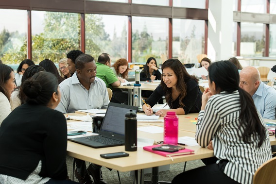 A group of people sitting and collaborating in a classroom type setting=