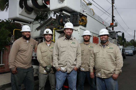 A group of men wearing nomex and hard hats looking at the camera