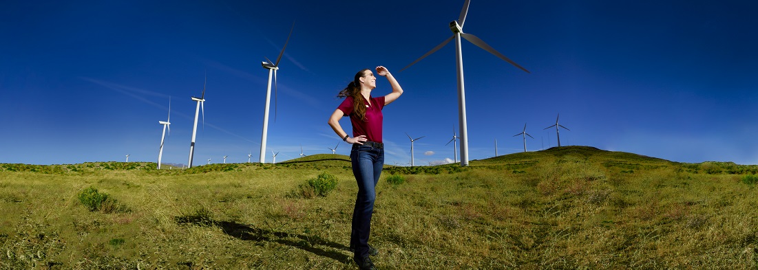 Woman standing in open grass land with wind turbines behind her
