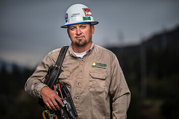 SCE utility worker with tools and hardhat with a forest in the background