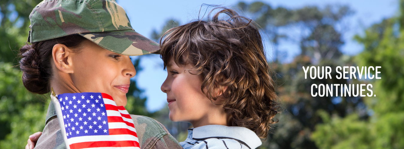 A military woman smiling and in uniform embracing a smiling child in her arms with a small United States flag and text Your service continues.