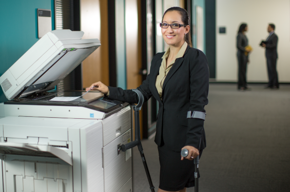 A woman smiling by the copy machine holding a cane and smiling into the camera