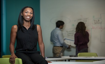 A smiling woman with people back writing on a board in the background