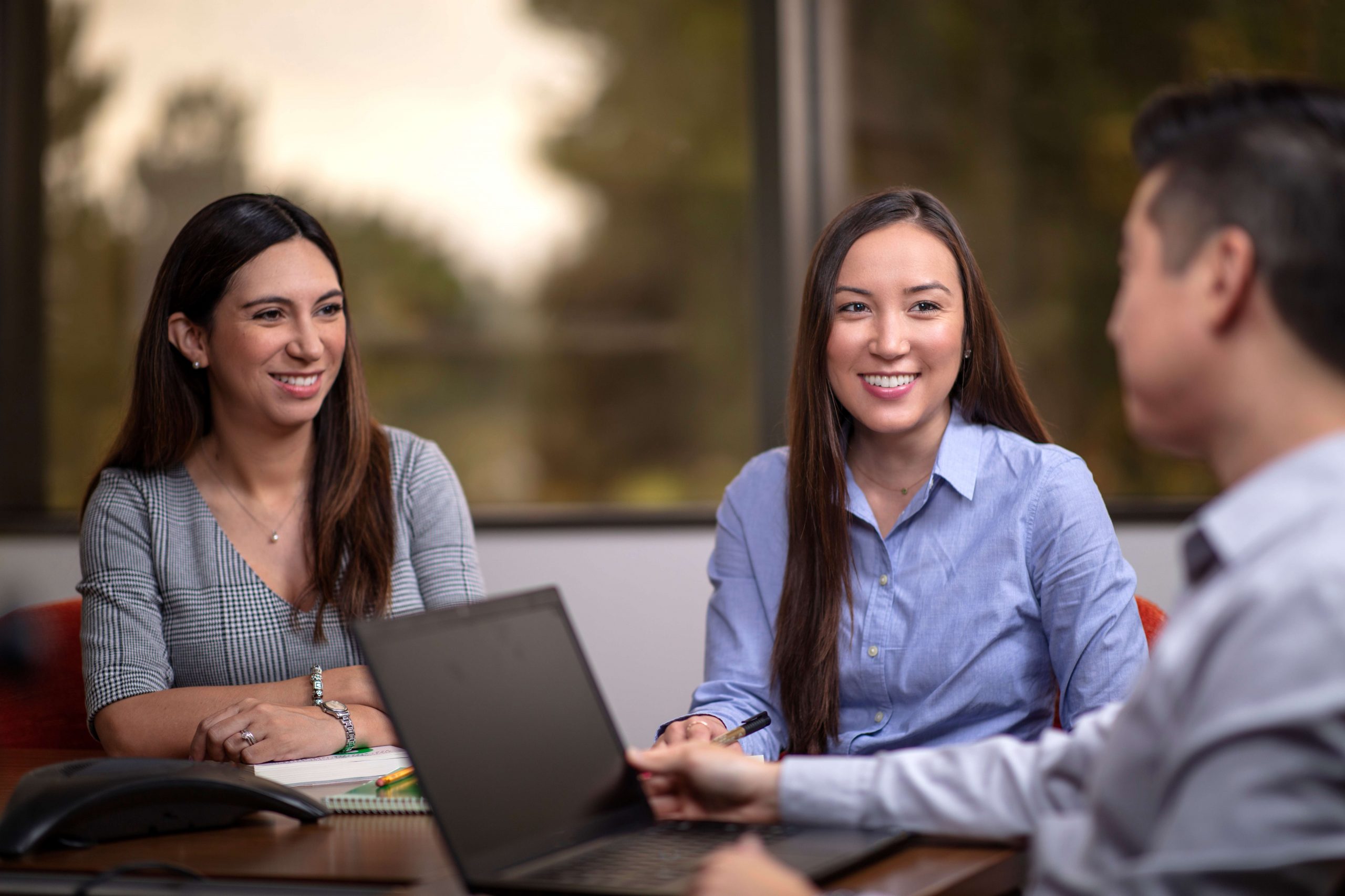 Two women smiling with a man on a laptop looking at them